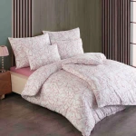 Pościel bawełniana 160x200 Cottonlove Exclusive Lenny w delikatny wzór roślinny w odcieniach różu. Zestaw składa się z kołdry i poduszek, leżących na łóżku z drewnianym zagłówkiem.