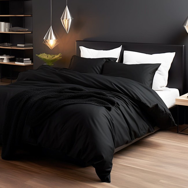 Poszewka satynowa 70x80 w kolorze czarnym, leżąca na łóżku z poduszkami; materiał o gładkiej fakturze, bez wzorów; otoczenie minimalistyczne, z lampami i rośliną w tle. Widzoczny również czarny koc na pościeli.