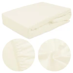 Prześcieradło frotte z gumką 60x120 w kolorze ecru, leżące, z widoczną fakturą materiału. W zbliżeniu szczegóły ściągacza na brzegach, które utrzymują prześcieradło na materacu. Tło neutralne, podkreślające kolor i strukturę tkaniny.