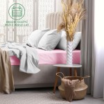 Prześcieradło frotte z gumką 60x120 w kolorze jasnego różu, rozłożone na łóżku, widoczne z boku. W otoczeniu szarej pościeli i jasnych poduszek, obok stolika z białym wazonem i dekoracjami. Tło neutralne, jasne, tworzy przytulną aranżację sypialni.