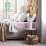 Prześcieradło frotte z gumką w kolorze wrzos na materacu, złożone w połączeniu z jasnoszarymi poszewkami na poduszki. Produkt leży płasko, tworząc elegancką aranżację łóżka. Na stoliku obok widoczny dekoracyjny wazon i kosz.