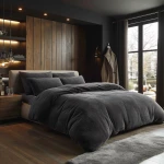 Pościel frotte 200x220 w kolorze antracytowym, leżąca na łóżku. Widoczna miękka faktura materiału i poduszki w tym samym odcieniu. Tło przedstawia nowoczesną sypialnię z drewnianą ścianą oraz dużymi oknami. W otoczeniu lampy i drewniane meble.