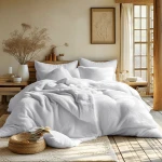 Pościel frotte 200x220 w kolorze białym, złożona na łóżku z poduszkami. W tle widoczna drewniana ściana, roślinność w wazonie oraz jasne zasłony, tworzące przytulny klimat. Na podłodze dywan i kosz z książkami.