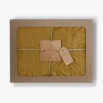 Pościel bawełniana w kolorze musztardowym, zapakowana w prostokątne, tekturowe pudełko z okienkiem. Widoczne falbany na krawędziach i metka z napisem „LIMASSO”. Produkt złożony, przymocowany sznurkiem. Tło jasne, neutralne.