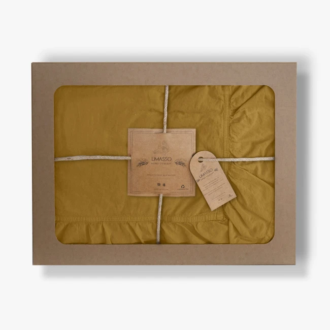 Pościel bawełniana w kolorze musztardowym, zapakowana w prostokątne, tekturowe pudełko z okienkiem. Widoczne falbany na krawędziach i metka z napisem „LIMASSO”. Produkt złożony, przymocowany sznurkiem. Tło jasne, neutralne.