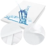 Ochraniacz na materac 120x200 Jason w kolorze białym, leżący na gładkiej powierzchni. Obrazek z efektem rozlania wody, podkreślający wodoodporność. Zbliżenia na fakturę materiału i detale brzegu, w tym elastyczne mocowanie.