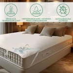 Ochraniacz na materac 70x140 Jason w kolorze białym, rozłożony na łóżku z jasnymi poduszkami. Widoczna impermeable faktura, ze wzorem zabezpieczającym przed zabrudzeniami. Na zdjęciu widoczne rozlane płyny, demonstrujące właściwości ochronne materaca.