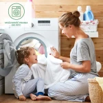 Mamy dwie osoby – kobietę w szarej koszulce i dziewczynkę w pasiastej pidżamie – w łazience przy pralce. Kobieta podaje białe ręczniki do bębna. Tło z drewnianych desek, widoczne środki piorące w pojemnikach. Pralka ma cyfrowy panel sterujący.