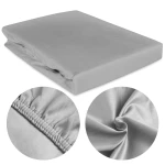 Prześcieradło satynowe z gumką w kolorze popielatym, złożone, z widoczną elastyczną krawędzią gumki. W zbliżeniu szczegóły faktury materiału, gładka powierzchnia, bez wzorów. Idealne na materac 180x200 cm, prezentowane na jasnym tle.