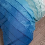 Pościel satyna bawełniana 200x220 w niebiesko-białe pasy, leżąca na jasnej podłodze. Materiał o delikatnej fakturze i subtelnym połysku. Wzór w odcieniach błękitu, z paskami o różnej grubości. Widoczna pościel z poduszkami, przyjemna dla oka aranżacja.