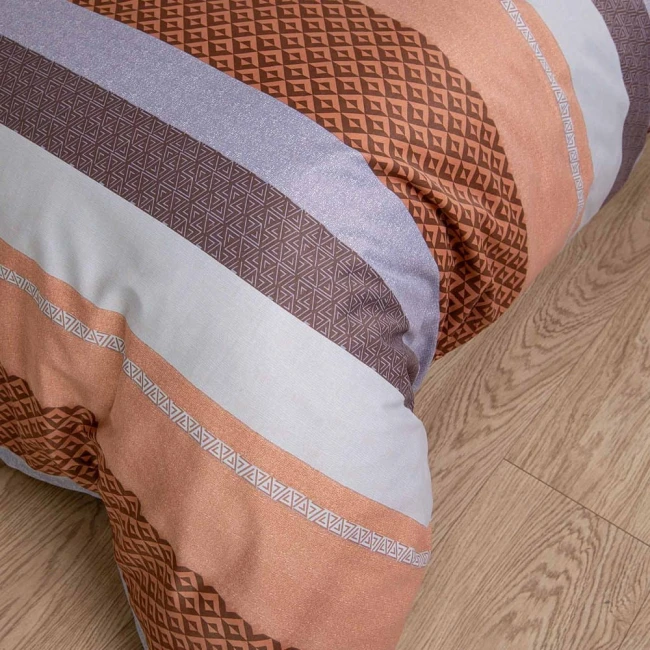 Pościel satyna bawełniana 160x200 w pomarańczowo-brązowe pasy z wzorem w geometryczne kształty. Ułożona poziomo, zbliżenie na fakturę materiału. Tło drewniane, podłogowe, bez dodatkowych elementów dekoracyjnych.