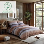 Pościel satynowa 160x200 w pomarańczowo-brązowe pasy, z poduszkami. Ułożona na łóżku w jasnej sypialni, z widocznym dekoracyjnym wzorem i teksturą. Tło z roślinami, oknem oraz naturalnym oświetleniem.