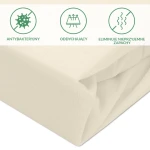 Ochronne prześcieradło z gumką 70x140 cm w kolorze kremowym. Materiał z fakturą, elastyczny brzeg. Właściwości: antybakteryjny, oddychający, eliminuje nieprzyjemne zapachy. Widok z boku, lekko złożone.