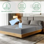 Ochronne prześcieradło z gumką 140x200 SMARTCEL w kolorze szarym, leżące na łóżku. Widoczne kropelki wody na materiale, obok szklanka z wylewającą się wodą.