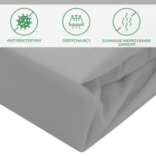 Ochronne prześcieradło z gumką o wymiarach 90x200 cm w kolorze szarym. Zbliżenie na materiał, podkreślające jego fakturę i gładkość. W tle widoczne symbole informujące o właściwościach antybakteryjnych, oddychających i eliminujących nieprzyjemne zapachy.