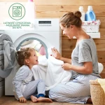 Kobieta w szarej koszulce i spodniach w pionowe paski siedzi na podłodze obok pralki, trzymając białe ręczniki. Obok niej, na podłodze, siedzi uśmiechnięta dziewczynka w piżamie w paski. Tło drewniane z koszem na pranie i detergentami.