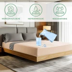 Ochronne prześcieradło z gumką 200x220 w kolorze beżowym, leżące na łóżku. Widoczne znaki graficzne informujące o właściwościach: nieprzepuszczalne, nieprzemakalne, wodoodporne. Tło w nowoczesnej aranżacji sypialni z szaro-beżowymi poduszkami.