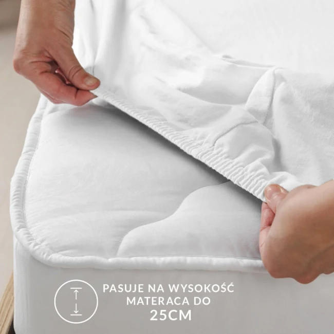 Ochronne prześcieradło z gumką w kolorze kremowym, o wymiarach 70x140, leżące na materacu, z widocznymi elastycznymi brzegami. Ujęcie zbliżone, pokazujące detale gumki. Napisy informujące o dopasowaniu do materaca o wysokości do 25 cm na jasnym tle.