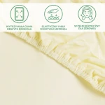 Ochronne prześcieradło z gumką 70x140 w kolorze kremowym, wykonane z miękkiego, elastycznego materiału. Widoczne jest obszycie gumką dookoła, co zapewnia stabilne dopasowanie. Tło jest jasne, co podkreśla detail produktu.