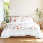 Pościel bawełniana 200x220 Cottonlove Exclusive Elyese w białym kolorze, ozdobiona kolorowymi, wiosennymi kwiatami. Produkt leżący na łóżku, ukazujący poszewki na poduszki oraz kołdrę. Tło jasne, naturalne światło, stylowy wystrój.