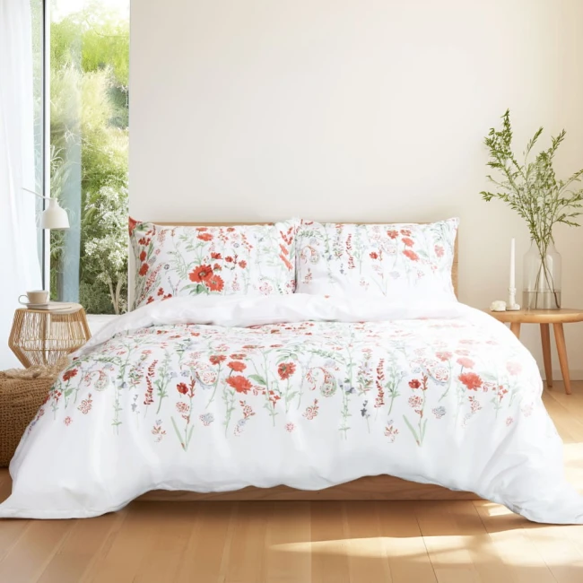 Pościel bawełniana 200x220 Cottonlove Exclusive Elyese w białym kolorze, ozdobiona kolorowymi, wiosennymi kwiatami. Produkt leżący na łóżku, ukazujący poszewki na poduszki oraz kołdrę. Tło jasne, naturalne światło, stylowy wystrój.