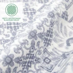 Pościel bawełniana Cottonlove Exclusive Pava w kolorze białym z niebieskim ornamentem, złożona w pół, ukazująca teksturę materiału. Wzór floralny z delikatnymi zdobieniami. Widoczne logo i napis, tylko w dolnej części zdjęcia, na jasnym tle.