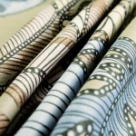 Pościel satyna bawełniana 220x200 w odcieniach zieleni, z dekoracyjnym wzorem liści. Tkanina gładka, stylizowana, widok z bliska na fałdy materiału, leżąca w złożeniu, na jednolitym tle.