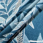 Pościel satyna bawełniana 220x200 w odcieniach niebieskiego, z subtelnym wzorem liści w jasnych tonacjach. Tkanina układa się w falach, eksponując delikatną fakturę materiału. Zdjęcie zbliżeniowe podkreśla detale rysunku oraz kolorystykę.