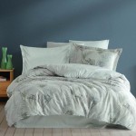 Pościel satyna bawełniana 220x200 w kolorze zielonym z dekoracyjnym wzorem liści palmowych. Zestaw składa się z poszwy na kołdrę oraz dwóch poszewek na poduszki. Produkt leżący na łóżku, na jasnym tle w przytulnym wnętrzu.