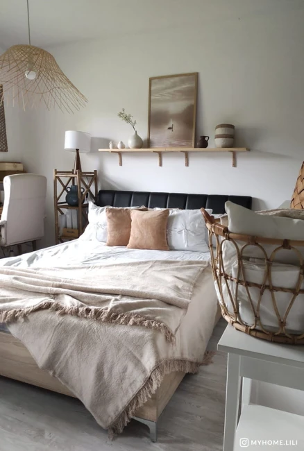 Koc bawełniany 200x220 cm w jasnym beżu, rozłożony na łóżku. Widoczne frędzle na krawędziach. Pościel z poszewkami w białym kolorze. Elementy aranżacji, takie jak drewniana półka i kosz, w tle. Prostokątny kształt koca, leżący na posłaniu.