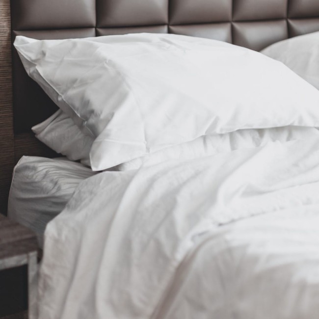 Prześcieradło bawełniane hotelowe w kolorze białym, rozłożone na łóżku. Widać jego gładką fakturę oraz kształt dopasowany do rozmiaru 160x240.