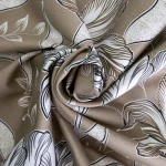 Pościel satyna bawełniana 160x200 w odcieniach brązu, zdobiona białymi kwiatami i liśćmi. Materiał gładki, z delikatnym połyskiem. Złożona w spirali, ukazując szczegóły wzoru. Tło jednolite, podkreślające wyrazistość grafiki.