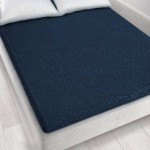 Prześcieradło żakardowe bez gumki w kolorze granatowym, o wymiarach 175x220 cm, leży na łóżku. Produkt ma delikatnie teksturowaną powierzchnię z wzorem, odsłonięty na jasnym tle podłogi. Widoczne są dwa poduszki.