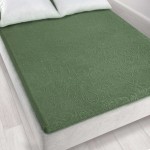 Prześcieradło żakardowe bez gumki w kolorze zielonym o wymiarach 175x220 cm, leżące na łóżku. Widoczne delikatne wzory na tkaninie, które nadają teksturę. Tło jasne, z poduszkami w białym przypadku, co podkreśla kolor prześcieradła.