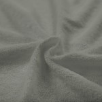 Poszewka frotte 40x40 w kolorze szarym, z miękką teksturą i delikatnym splotem, leży na tle w odcieniach szarości, układając się w falującą formę. Widoczne różnice w strukturze materiału podkreślają jego funkcję dekoracyjną i użytkową.