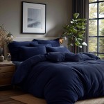 Poszewka frotte 40x40 w ciemnym granacie, leżąca na łóżku w aranżacji sypialni. Widoczne różne rozmiary i kształty poduszek w tym samym kolorze na tle jasnej ściany. W tle lampa oraz roślina doniczkowa przy oknie.