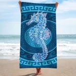Ręcznik plażowy 100x180 cm wykonany z mikrofibry, z motywem konika morskiego w odcieniach błękitu, na wzorzystym tle. Produkt trzymany w pozycji stojącej nad brzegiem morza, widoczny detal graficzny konika morskiego oraz okrągły wzór dekoracyjny.
