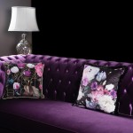 Fioletowa poszewka dekoracyjna 43x43 cm z frędzlami, zdobiona kolorowymi kwiatami na czarnym tle. Produkt leży na ciemnofioletowej kanapie. Widać wyraźny wzór floralny oraz dekoracyjne brzegi, co podkreśla elegancki charakter aranżacji.