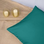 Poszewka satynowa 50x70 w kolorze ciemnego turkusu, leżąca na jasnym tle. Gładka faktura materiału, skoszony brzeg, obok dwa złote świeczniki z białymi świecami. Ujęcie w zbliżeniu na produkt, eksponujące intensywny kolor i połysk.