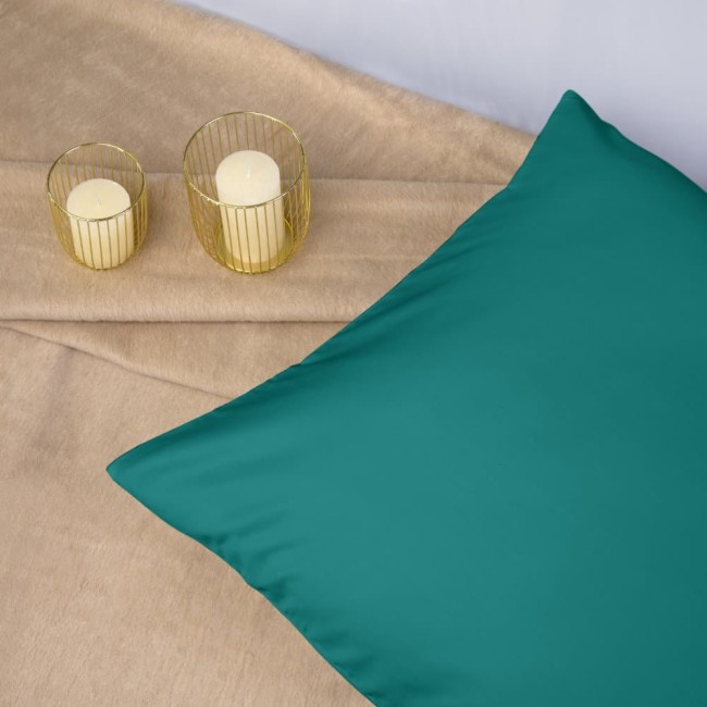 Poszewka satynowa 50x70 w kolorze ciemnego turkusu, leżąca na jasnym tle. Gładka faktura materiału, skoszony brzeg, obok dwa złote świeczniki z białymi świecami. Ujęcie w zbliżeniu na produkt, eksponujące intensywny kolor i połysk.