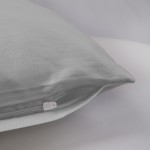 Poszewka satynowa 50x70 w kolorze popielatym, leżąca na jasnym tle, z widocznym białym zamkiem. Materiał gładki, z drobną fakturą. Produkt ukazany w zbliżeniu na detal brzegów oraz zamka, co podkreśla jakość wykonania.