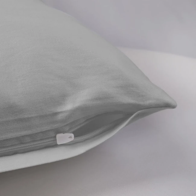Poszewka satynowa 50x70 w kolorze popielatym, leżąca na jasnym tle, z widocznym białym zamkiem. Materiał gładki, z drobną fakturą. Produkt ukazany w zbliżeniu na detal brzegów oraz zamka, co podkreśla jakość wykonania.
