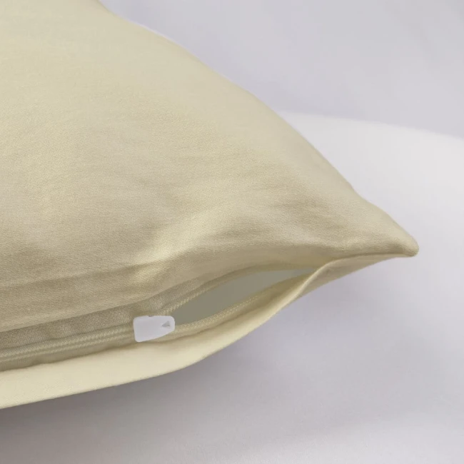 Poszewka satynowa 50x70 w kolorze kremowym, leżąca na białym tle, z widocznym zamkiem błyskawicznym. Materiał gładki, błyszczący, o delikatnej strukturze. Ujęcie z boku, pokazujące kształt i krawędzie poszewki.