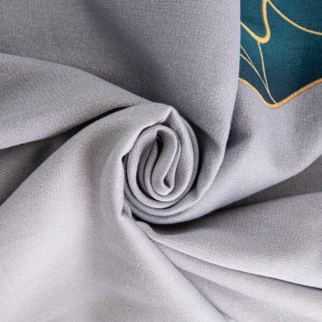 Satynowa pościel w kolorze szarym, zwinięta w roladę, z zielonymi liśćmi na widocznej krawędzi. Materiał o gładkiej teksturze, zasłaniający szczegóły wzoru. Zestaw przeznaczony do łóżka o wymiarach 140x200 cm.