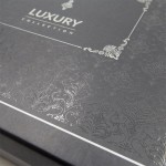 Pościel satyna bawełniana żakardowa 160x200 w eleganckim opakowaniu z szarego kartonu. Na wierzchu widoczny detal w formie srebrzystego haftu z ozdobnym wzorem oraz napisem LUXURY COLLECTION. Opakowanie leży poziomo, prezentując gładką fakturę.