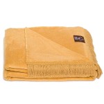 Koc bawełniany w kolorze miodowym o wymiarach 150x200 cm, z frędzlami na krótszym boku. Zwinięty, z widocznym logo w lewym dolnym rogu. Tło zdjęcia jasne. Koc o gładkiej, miękkiej fakturze, idealny do użytku domowego.