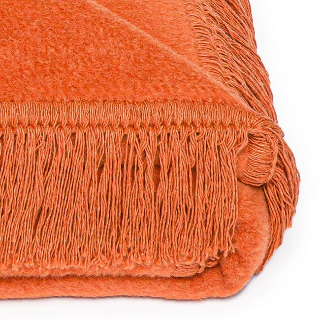 Koc bawełniany 150x200 cm w intensywnym pomarańczowym kolorze, z frędzlami na brzegach. Dodany w widoku z góry, leżący na białym tle, prezentujący teksturę materiału oraz staranne wykończenie.