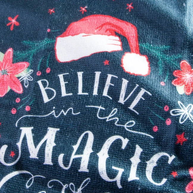 Ścierka kuchenna w komplecie 2 sztuk, kolor ciemnoniebieski, z nadrukiem Świętego Mikołaja oraz napisem BELIEVE in the MAGIC. Wzór otoczony czerwonymi kwiatami i zielonymi gałązkami, materiał tekstylny, wymiar 38x60 cm. Złożona, widok frontalny.