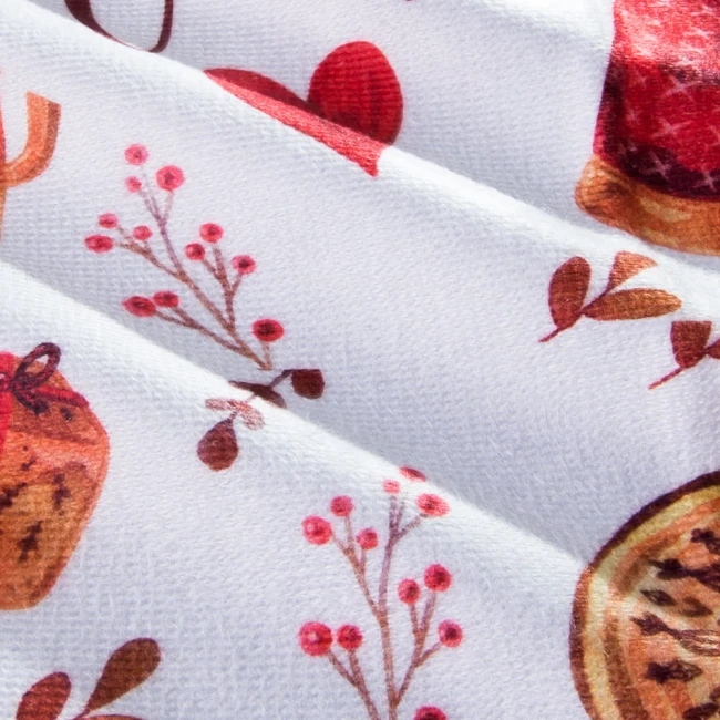 Ścierka kuchenna Christmas w kolorze bieli z zielonymi i czerwonymi wzorami bożonarodzeniowymi, takimi jak owoce, gałązki i ciasta. Produkt leży na płasko, ukazując teksturę materiału i detale nadruku. Wymiary 38x60 cm.