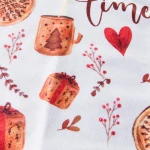 Ścierka kuchenna w kolorze białym z zielonymi i czerwonymi dekoracjami, przedstawiająca świąteczne motywy: kubek z choinką, prezenty, gałązki i serce. Złożona, z wyraźnym nadrukiem, ukazana z bliska na jednolitym tle. Wymiary 38x60 cm.